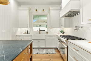 Kitchen featuring custom range hood, double oven range, backsplash, and sink