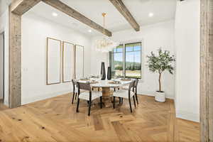 Dining room with a notable chandelier, beamed ceiling, and light parquet flooring