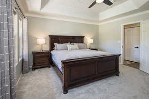 Carpeted bedroom featuring ceiling fan, ornamental molding, and a tray ceiling