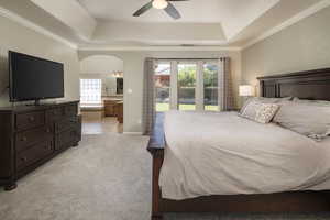 Bedroom featuring ceiling fan, a tray ceiling, crown molding, light colored carpet, and connected bathroom