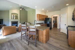 Kitchen featuring a kitchen breakfast bar, ceiling fan, wood-type flooring, black fridge, and sink