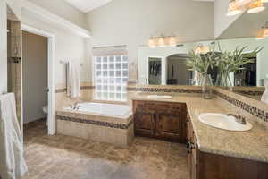 Bathroom featuring a towering ceiling, dual vanity, toilet, tile floors, and tiled bath