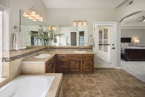 Bathroom with tile flooring, a relaxing tiled bath, dual bowl vanity, and ceiling fan