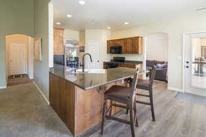 Kitchen featuring kitchen peninsula, black appliances, light carpet, sink, and a breakfast bar