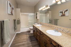 Full bathroom with double sink, oversized vanity, hardwood / wood-style floors, tiled shower / bath combo, and toilet