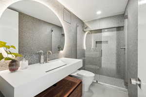 Bathroom featuring a tile shower, vanity, toilet, and tile walls