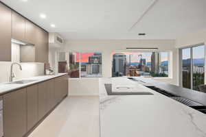 Interior space with hanging light fixtures, gray cabinetry, light stone countertops, sink, and light tile floors