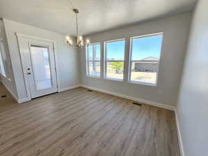 Unfurnished dining area featuring a healthy amount of sunlight, an inviting chandelier, hardwood / wood-style flooring, and a textured ceiling