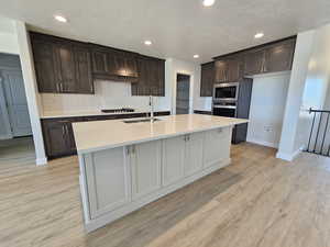 Kitchen featuring an island with sink, sink, appliances with stainless steel finishes, and light wood-type flooring