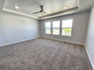 Carpeted spare room with a textured ceiling, ceiling fan, and a raised ceiling