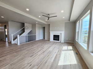 Unfurnished living room with a raised ceiling, ceiling fan, and light hardwood / wood-style flooring