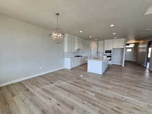 Kitchen with light hardwood / wood-style floors, white cabinets, and a center island with sink