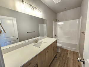 Full bathroom with toilet, tub / shower combination, wood-type flooring, vanity, and a textured ceiling