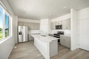 Kitchen featuring sink, appliances with stainless steel finishes, light hardwood / wood-style flooring, and an island with sink