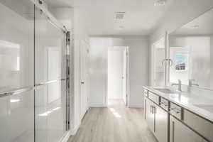 Bathroom featuring dual bowl vanity, hardwood / wood-style floors, an enclosed shower, and a textured ceiling