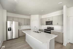 Kitchen featuring stainless steel appliances, light wood-type flooring, sink, a kitchen island with sink, and gray cabinetry