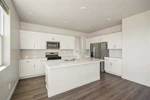 Kitchen featuring dark hardwood / wood-style flooring, white cabinets, sink, a center island with sink, and appliances with stainless steel finishes