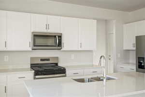 Kitchen with sink, white cabinetry, light stone counters, and stainless steel appliances