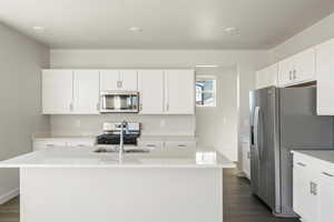 Kitchen with white cabinets, dark wood-type flooring, appliances with stainless steel finishes, and a center island with sink