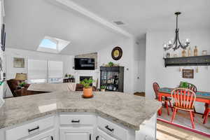 Kitchen with lofted ceiling with skylight, pendant lighting, white cabinets, light wood-type flooring, and an inviting chandelier