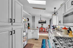 Kitchen featuring white cabinetry, light wood-type flooring, stainless steel appliances, pendant lighting, and sink