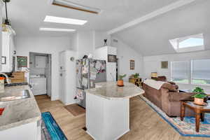 Kitchen with stainless steel fridge, light hardwood / wood-style floors, decorative light fixtures, washer / clothes dryer, and a skylight