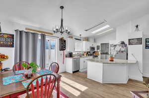 Kitchen with stainless steel appliances, vaulted ceiling, white cabinets, pendant lighting, and light wood-type flooring