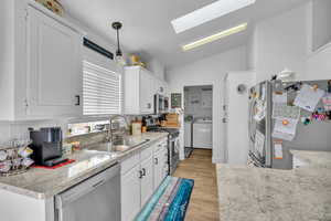 Kitchen featuring stainless steel appliances, sink, hanging light fixtures, light wood-type flooring, and lofted ceiling with skylight