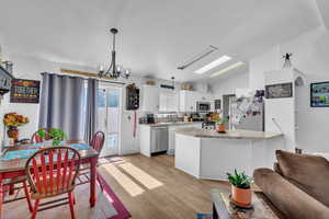 Kitchen with appliances with stainless steel finishes, white cabinets, pendant lighting, light wood-type flooring, and lofted ceiling