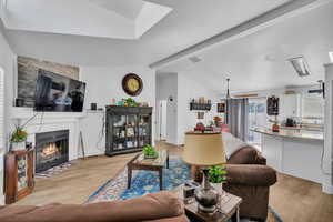 Living room with light hardwood / wood-style floors, a tiled fireplace, and lofted ceiling with beams