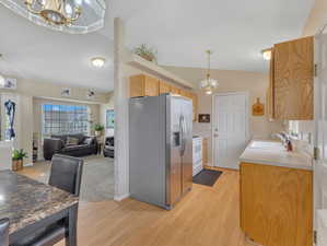 Kitchen with vaulted ceiling, an inviting chandelier, stainless steel fridge, sink, and pendant lighting