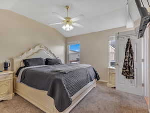 Carpeted bedroom with multiple windows, ceiling fan, and lofted ceiling