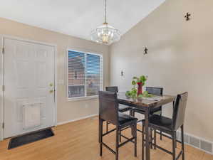 Dining space with light hardwood / wood-style floors, a notable chandelier, and vaulted ceiling