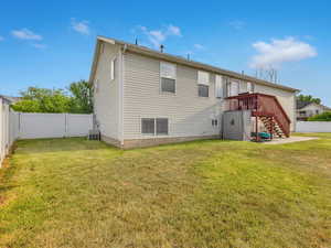 Back of property with a lawn, a deck, and central AC unit