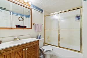 Full bathroom with tile flooring, a textured ceiling, combined bath / shower with glass door, vanity, and toilet