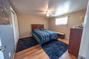 Bedroom featuring ceiling fan, a closet, brick wall, and laminate flooring.