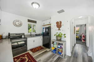 Kitchen with black fridge, sink, stainless steel range with electric stovetop, and hardwood / wood-style floors