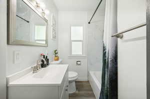 Full bathroom with hardwood / wood-style floors, oversized vanity, plenty of natural light, shower / bath combo, and toilet