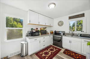 Kitchen with white cabinetry, sink, electric range, and light wood-type flooring