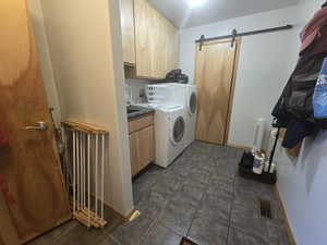 Laundry room featuring dark tile flooring, washer and clothes dryer, a barn door, and cabinets