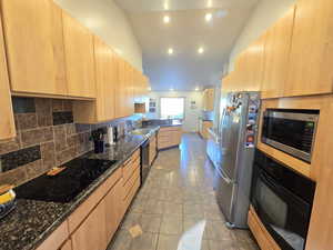 Kitchen with dark stone countertops, black appliances, light brown cabinetry, and tasteful backsplash