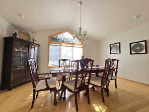 Dining room with light wood-type flooring, vaulted ceiling, and an inviting chandelier