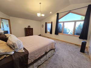 Carpeted bedroom with a notable chandelier and vaulted ceiling