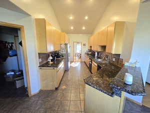 Kitchen featuring dark stone counters, tasteful backsplash, kitchen peninsula, and light brown cabinets