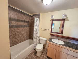 Full bathroom featuring a textured ceiling, tile floors, shower / tub combo with curtain, vanity, and toilet