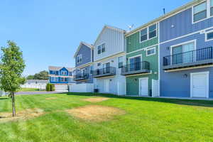 Rear view of property featuring a garage, a lawn, and a balcony