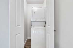 Clothes washing area featuring dark wood-type flooring and stacked washing maching and dryer