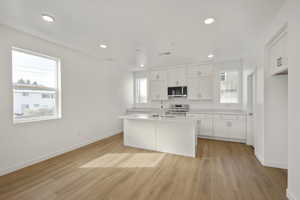 Kitchen featuring light wood-type flooring, sink, a kitchen island with sink, white cabinetry, and appliances with stainless steel finishes