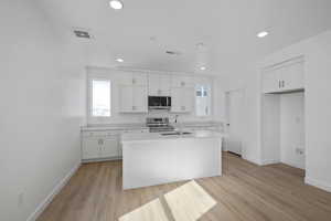 Kitchen featuring a kitchen island with sink, white cabinetry, light wood-type flooring, appliances with stainless steel finishes, and sink