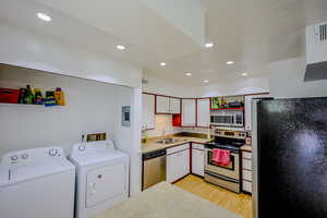 Kitchen with light hardwood / wood-style flooring, stainless steel appliances, washer and dryer, sink, and white cabinetry